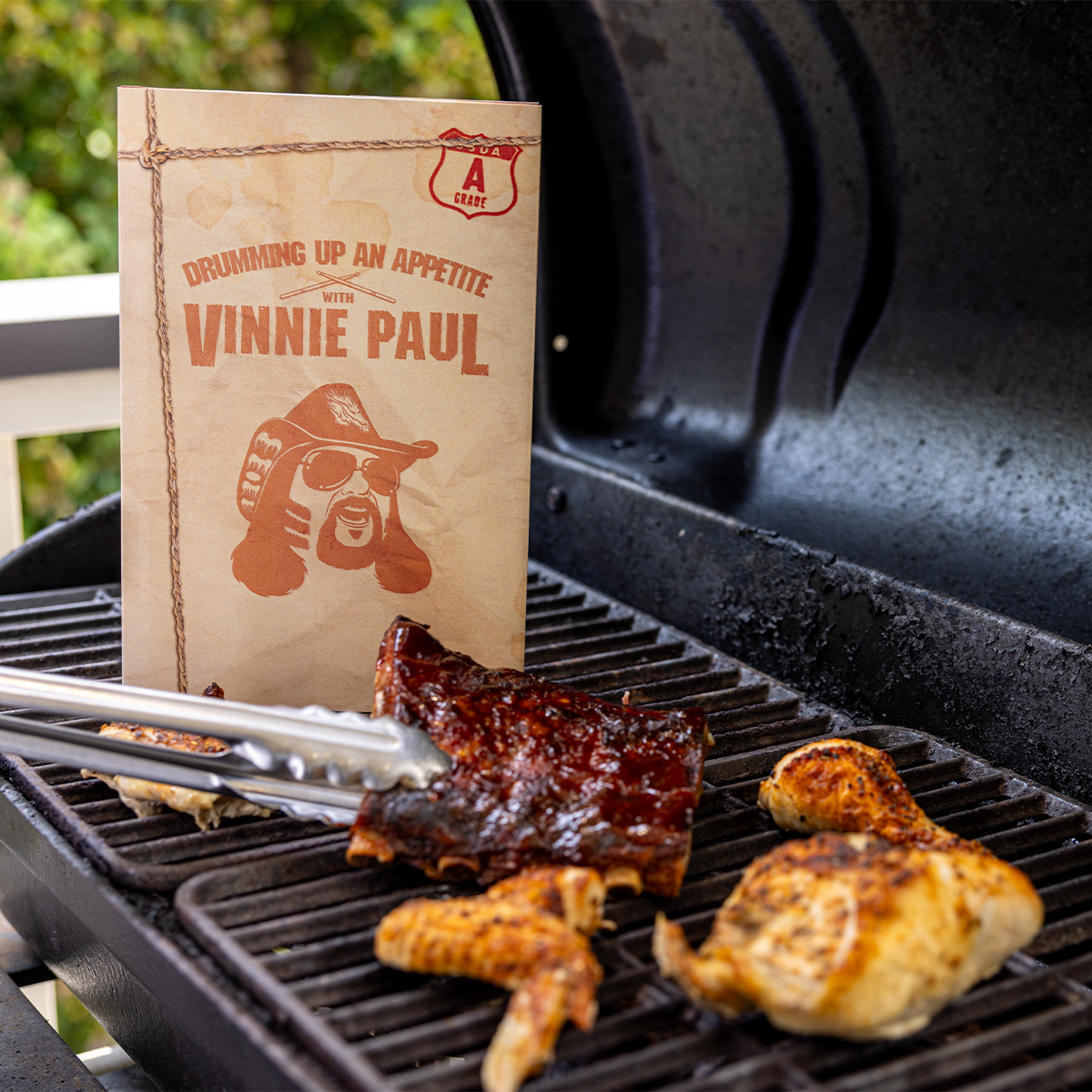 Grilled chicken and ribs on a barbecue with a 'Vinnie Paul' branded book.