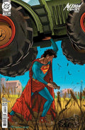 Superman holding a gun with large tires and a building in the background on a comic book cover.